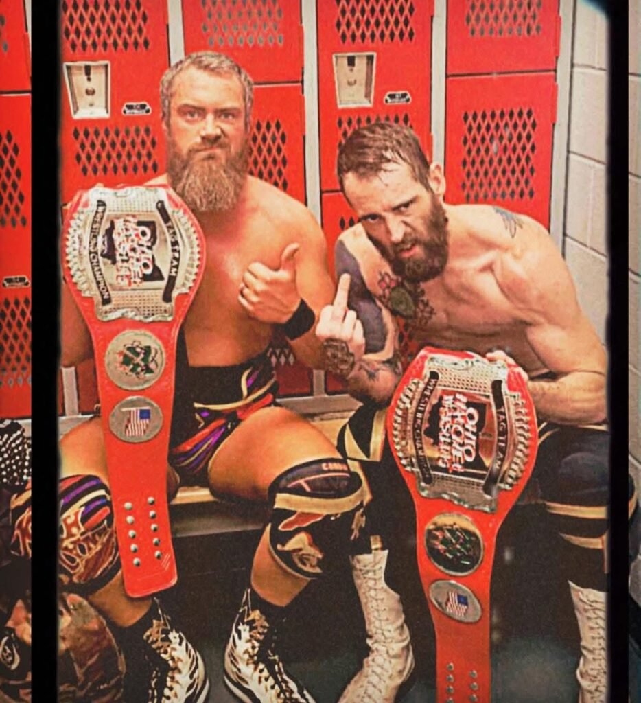 Two professional champs hold the wrestling championship belt that are crafted by the Absolute Belts.