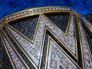 Close-up of WWE World Heavyweight Championship replica belt center plate with gold plating, clear stones and red accents